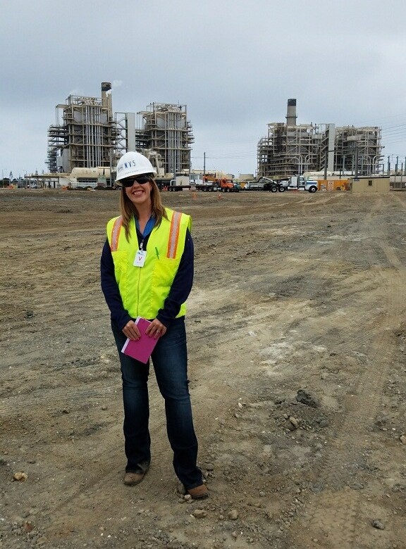 Person wearing a hard hat and high-visibility vest standing at an industrial power plant construction site.