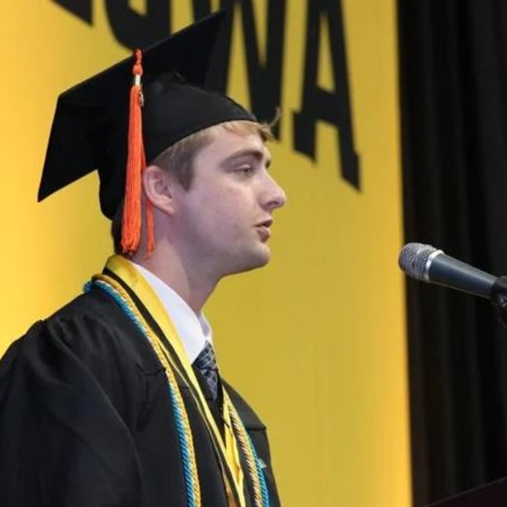 A person wearing a cap and gown speaking into a microphone