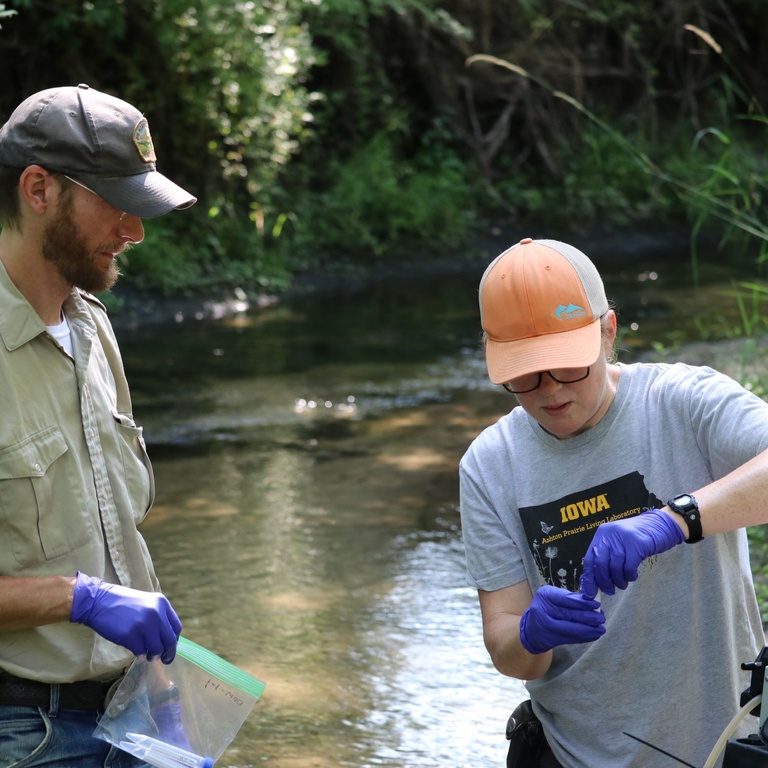 Two people collect samples from a creek