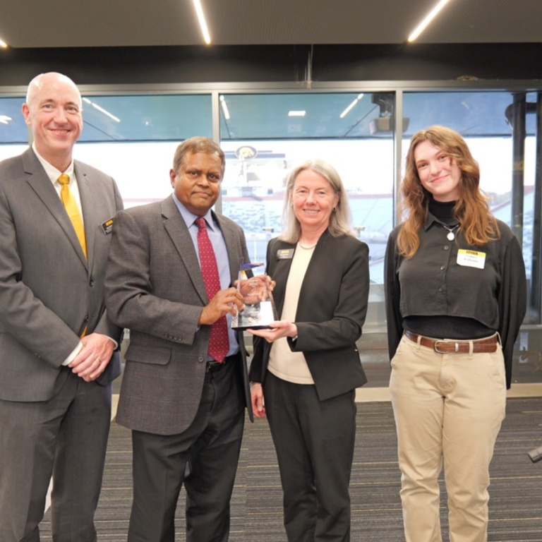 Man (second from left) holds trophy with three people by his side