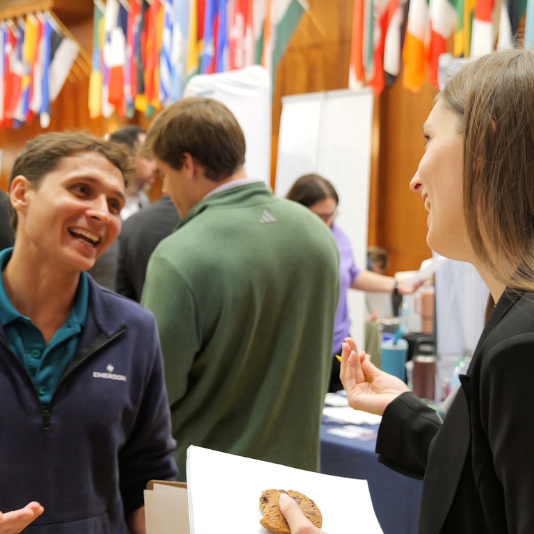 A student speaks with an employer representative during the Engineering Career Fair while other students and recruiters meet at booths beneath rows of international flags in the Iowa Memorial Union.