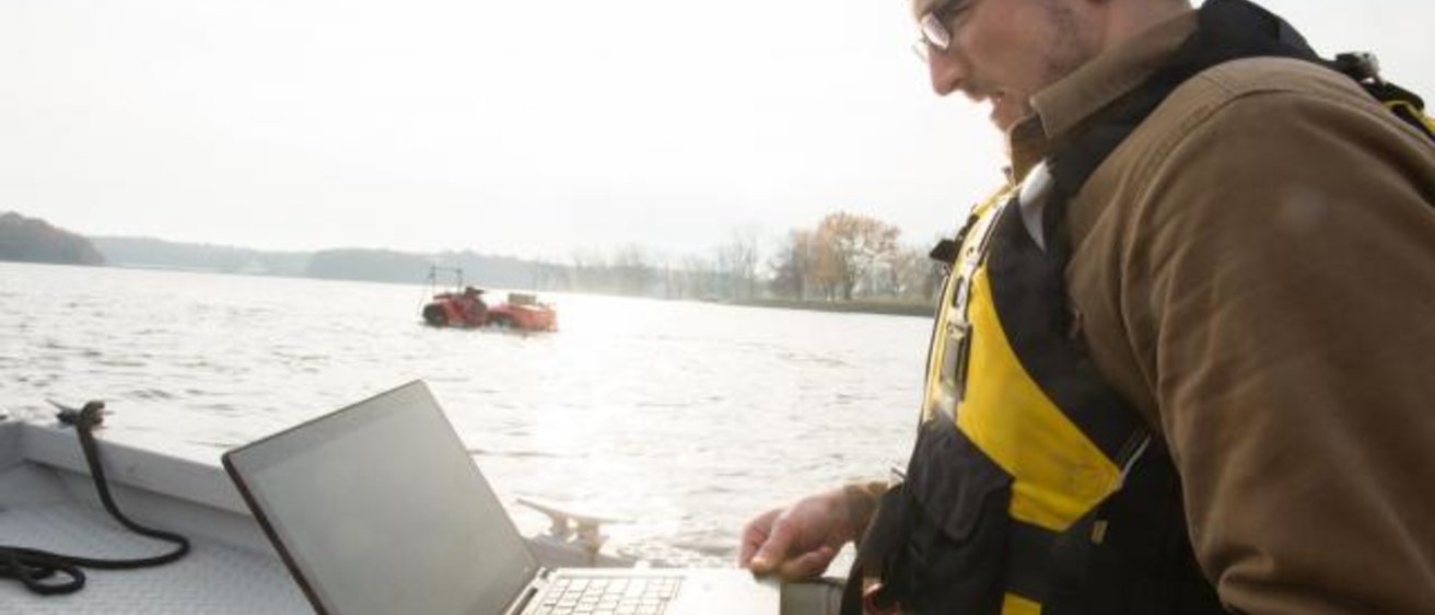 Casey Harwood working at his laptop in front of a river 