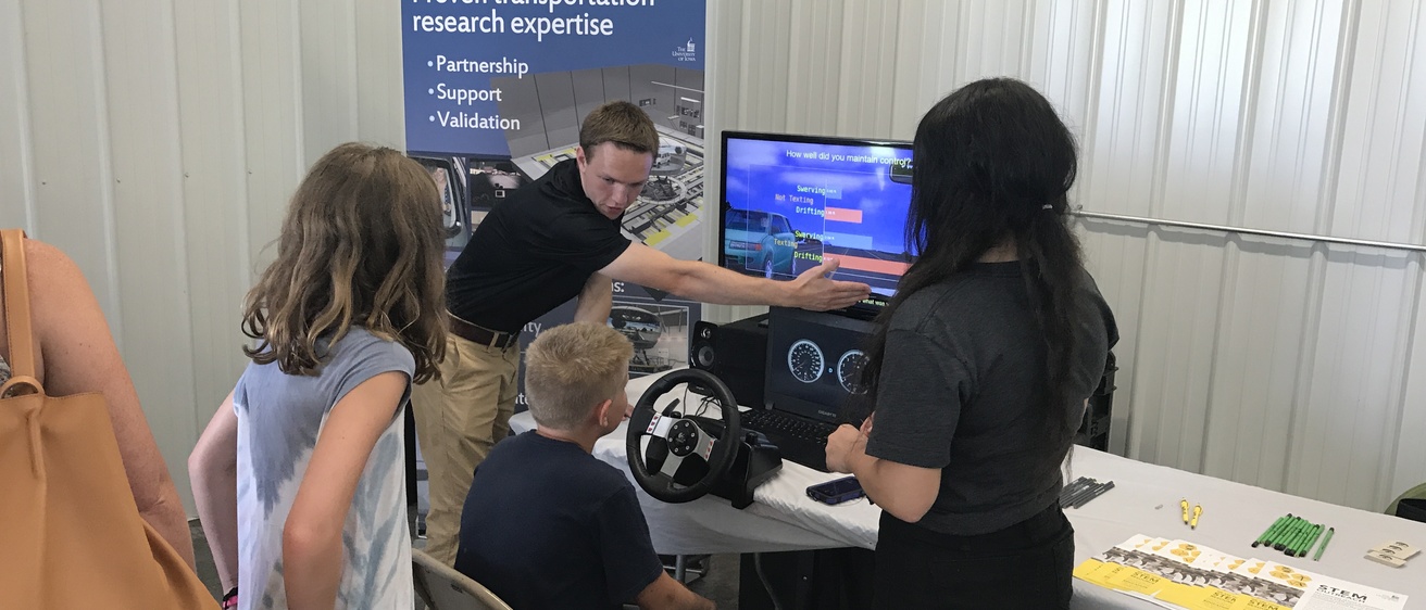 A staff member for the National Driving Simulator presenting the simulator to children