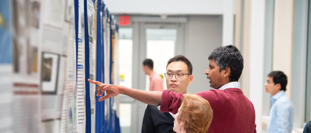 graduate students pointing at a research poster in a well lit hallway in the seamans center