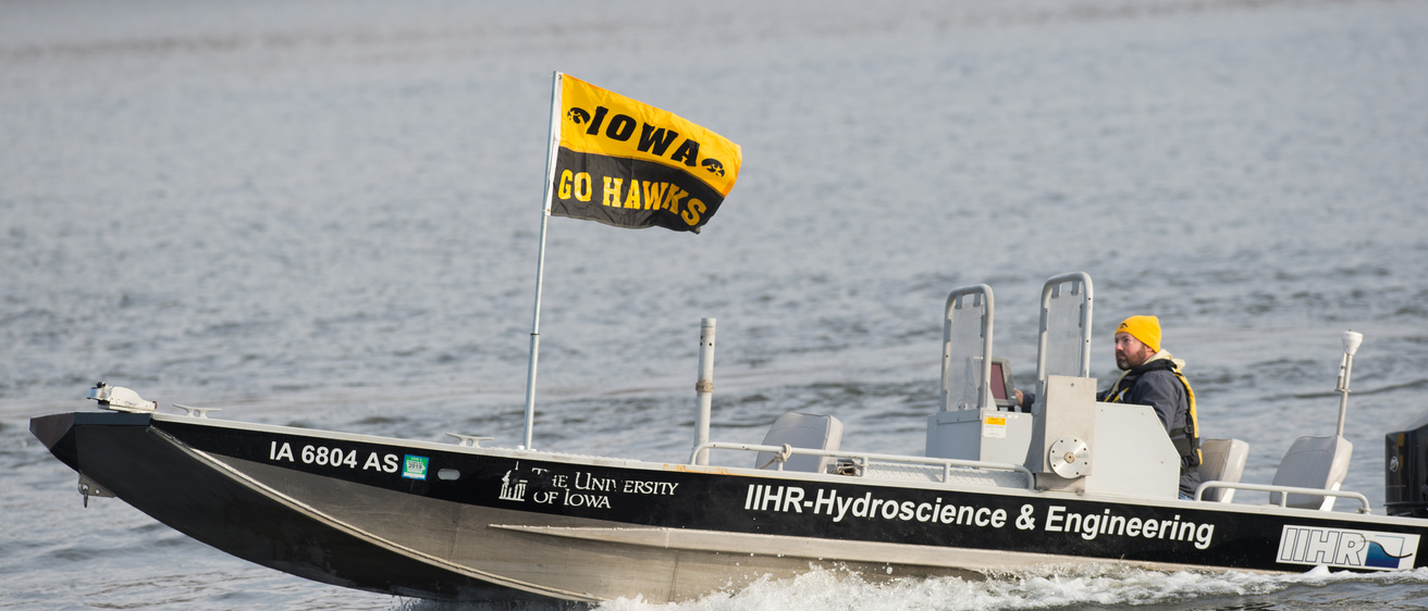 a boat with a gold and black Iowa flag cruising on a river