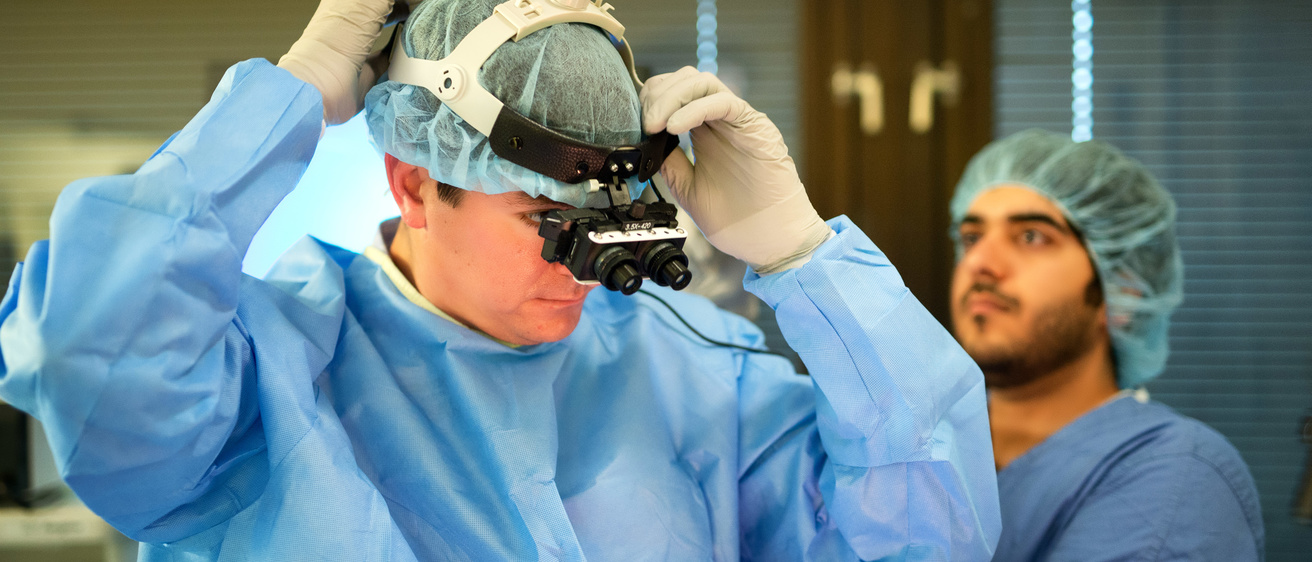 a man in a blue surgical gown adjusts metal smart goggles
