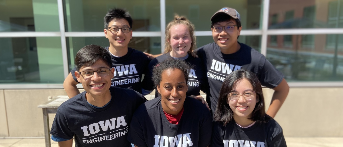 6 students in black iowa engineering tshirts pose in front of the seamans center