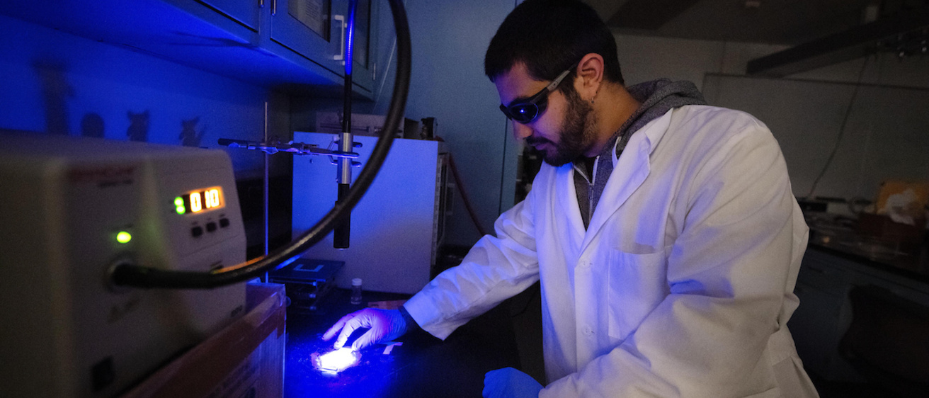 A student wearing goggles and working with photo polymerization in the lab