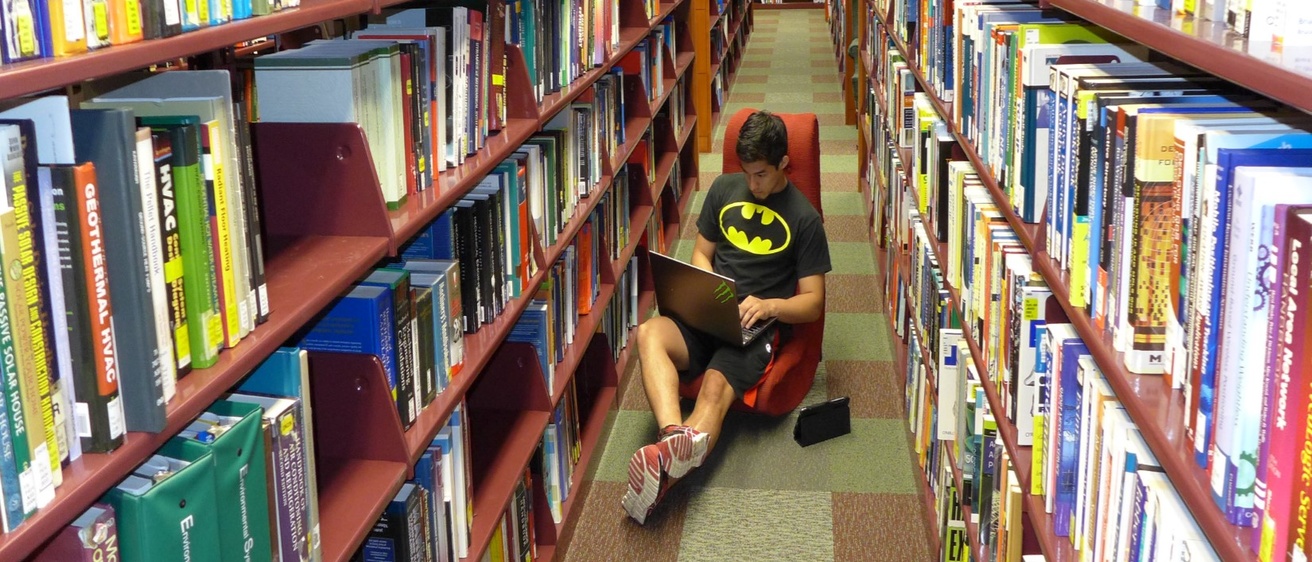 A person wearing a Batman t-shirt reads in the library stacks