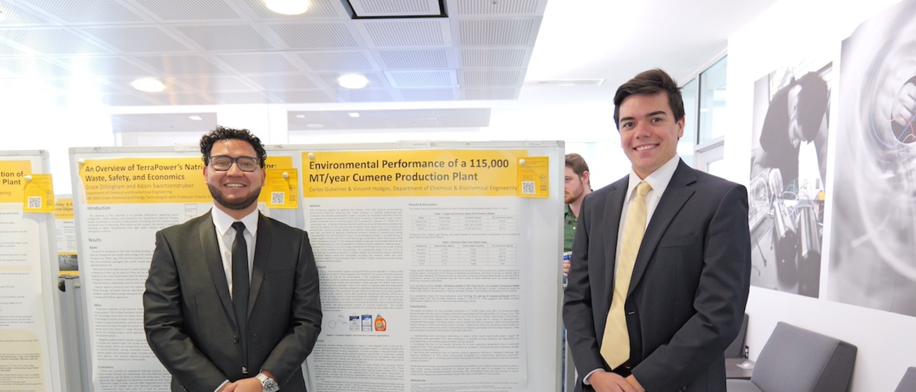 Two people pose by a research poster