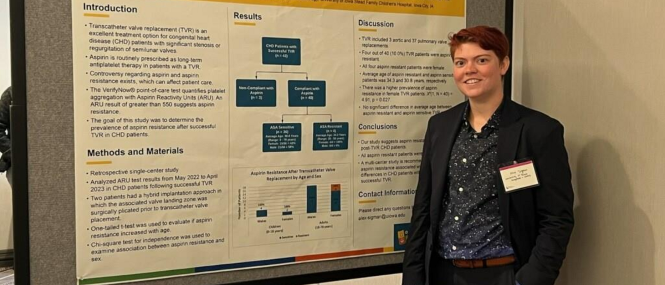 Person with dark clothing and short reddish hair stands to the right of a research poster