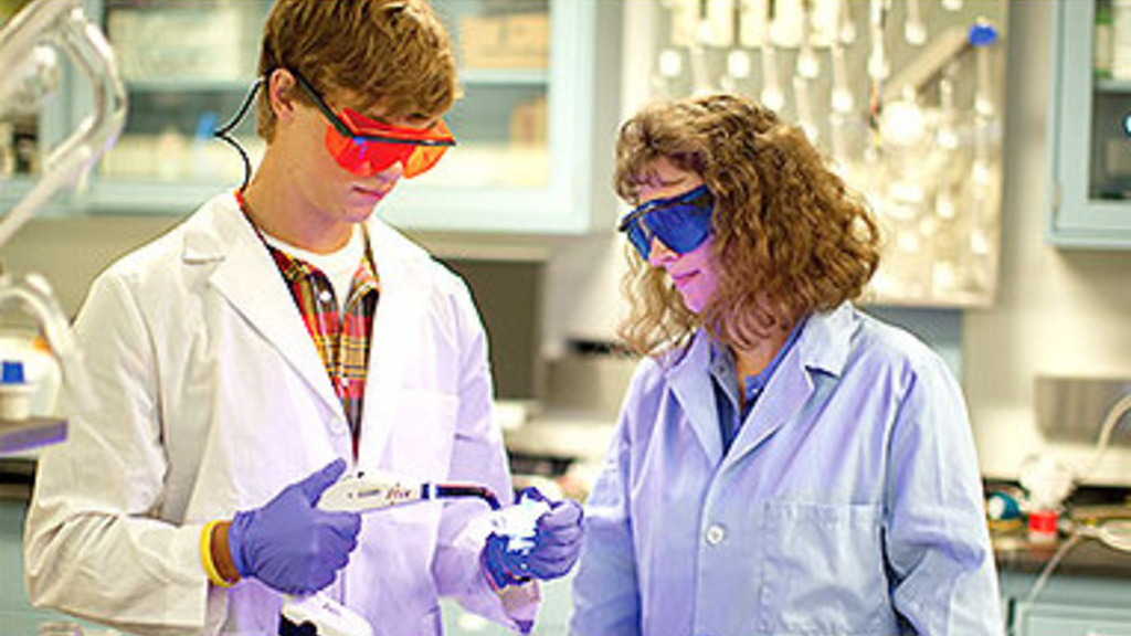 Student and a professor wearing lab coats and goggles