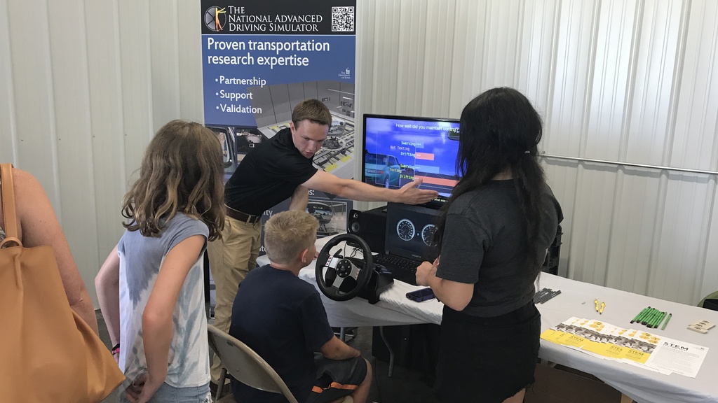 A staff member for the National Driving Simulator presenting the simulator to children