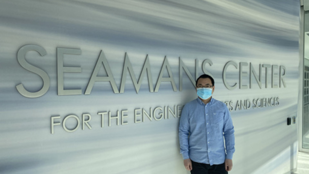 Qing Zou wearing a mask and standing inside the seamans center building entrance