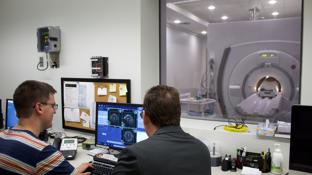 CBIG Lab, two men sitting looking at computer monitors that have scans of brains on them. a large mri machine is in the background