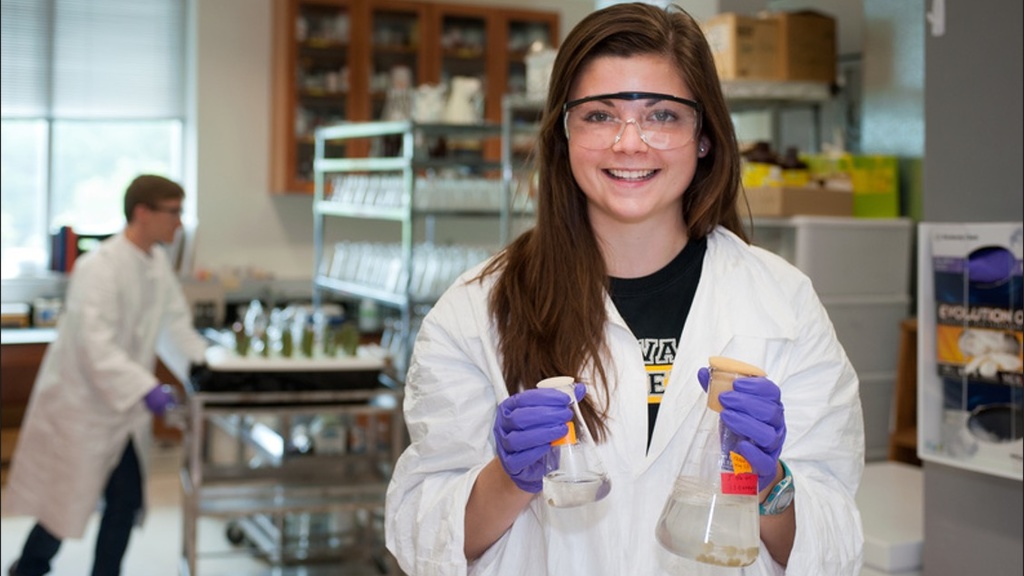 female student smiling wearing white lab coat and holding a chemistry beaker