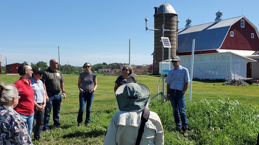 A group of people talk with a barn and silo in the background