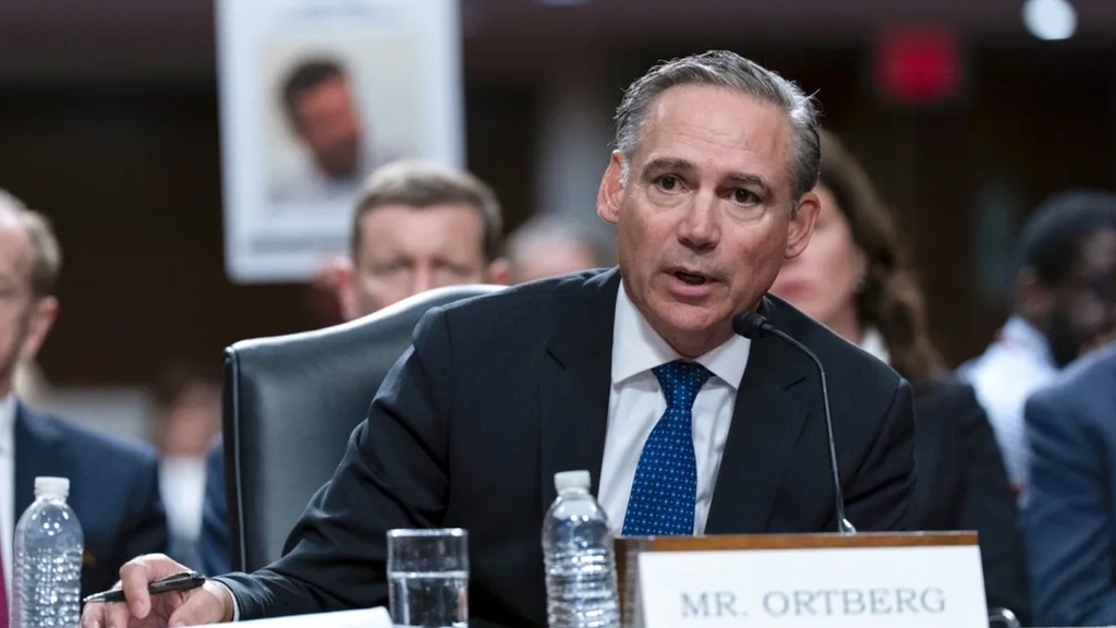 Kelly Ortberg speaks into a microphone at a table