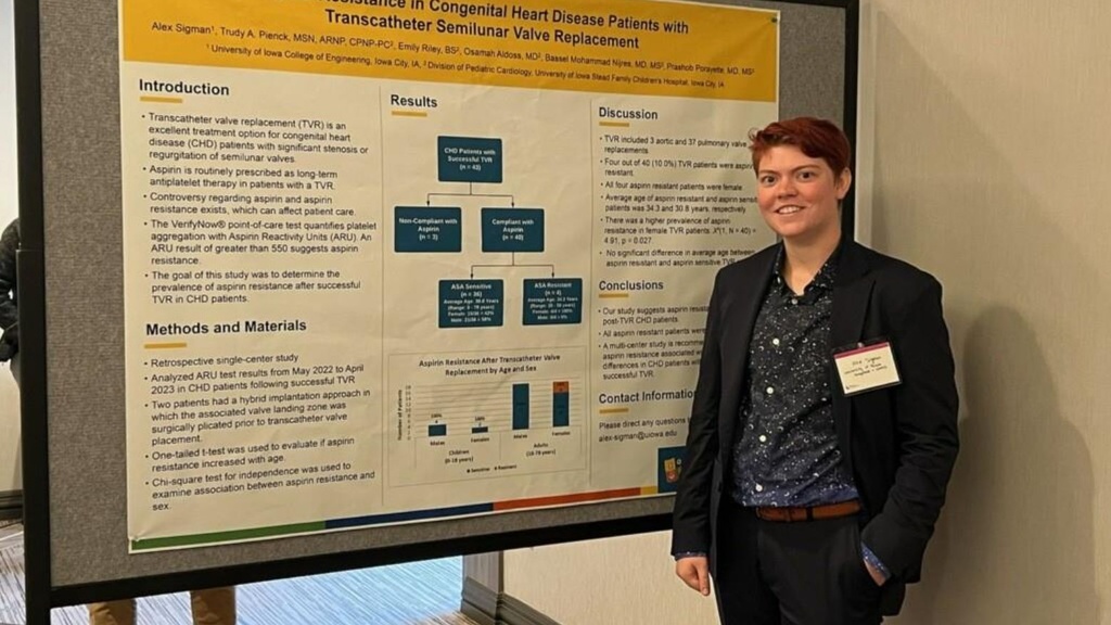 Person with dark clothing and short reddish hair stands to the right of a research poster