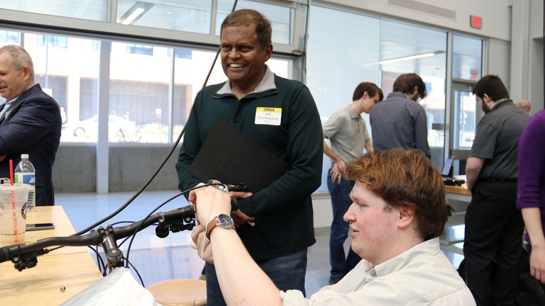 People gather around a workbench during a hands-on demonstration in a large indoor innovation space.