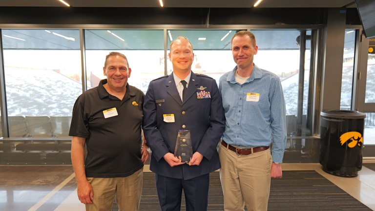 Three attendees pose with an award at a recognition event overlooking Kinnick Stadium.