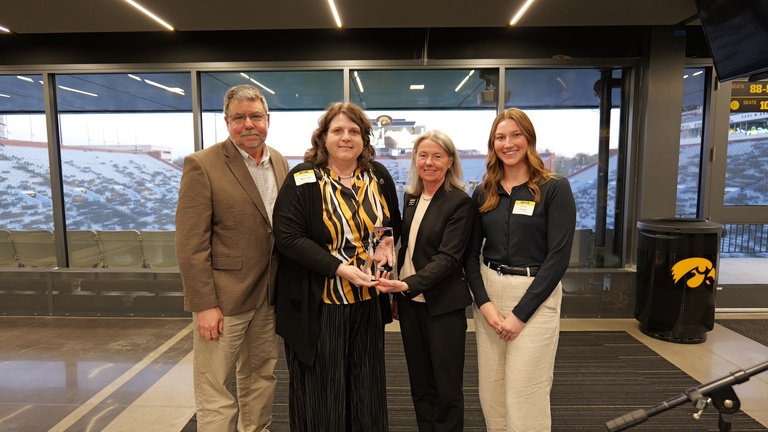 Award recipient poses with three others while displaying an award during the honored alumni recognition ceremony at Kinnick Stadium.