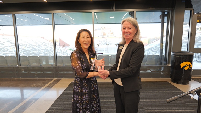 Recipient accepts an award during a recognition ceremony with Kinnick Stadium visible in the background.